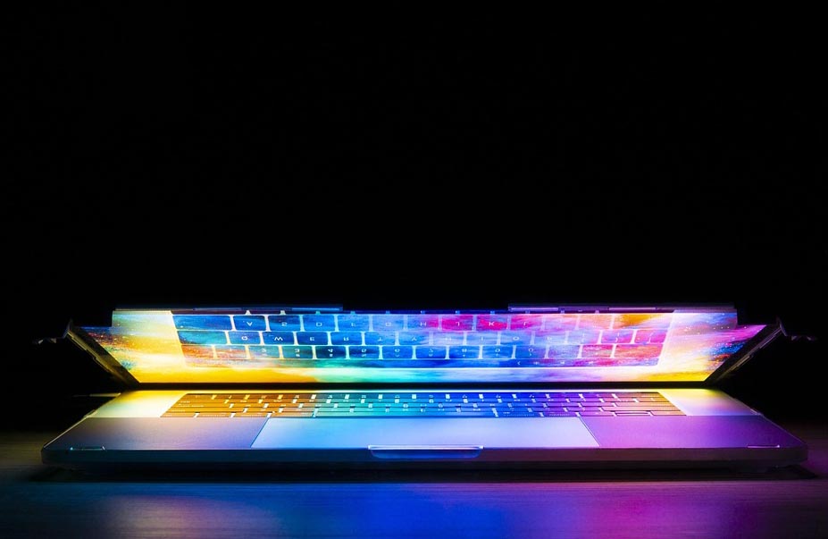 Webdesign für Magier:innen: Das Bild zeigt einen halb aufgeklappten Laptop vor schwarzem Hintergrund, mit psychedelischen Farben, die vom Bildschirm leuchten.